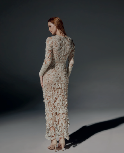 Modelo de frente luciendo el Vestido Eli largo de crochet color arena, de manga larga con flores inspiradas en el toborochi, en un estudio de fondo oscuro.