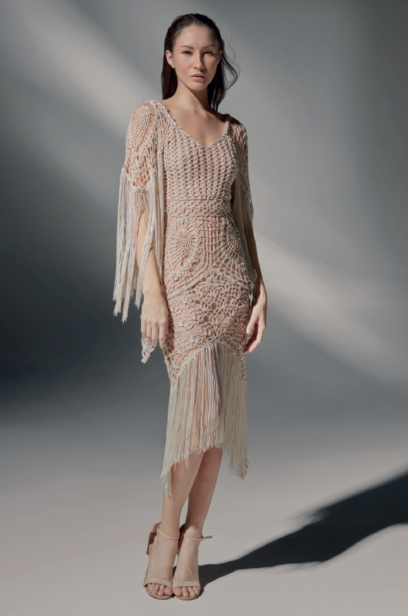 Modelo luciendo el Vestido Mica corto de crochet color arena, con escote en V y manga larga con flecos, en un estudio de fondo neutro.