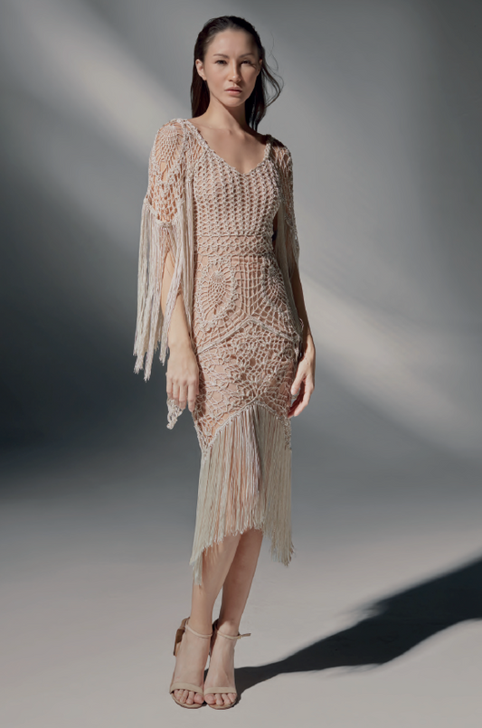 Modelo luciendo el Vestido Mica corto de crochet color arena, con escote en V y manga larga con flecos, en un estudio de fondo neutro.